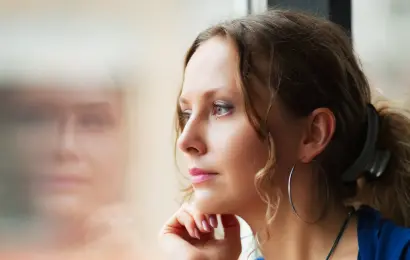 Woman looking out a window in quiet reflection, representing mindset shifts and personal growth at the start of a new year.