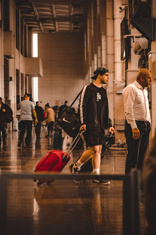 Traveler pulling a red suitcase through an airport terminal, illustrating carry-on luggage problems and unexpected airline baggage fees.