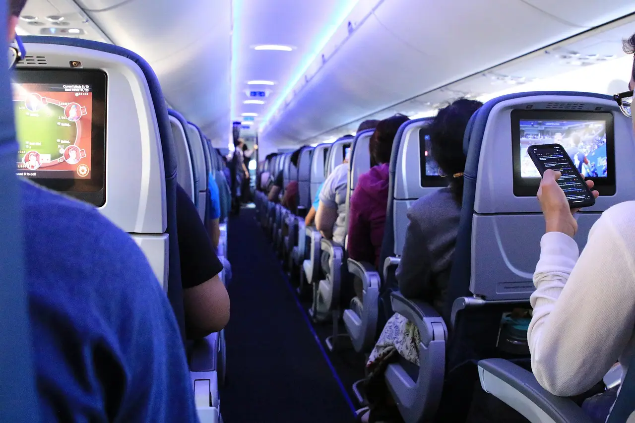 Passengers using smartphones and screens inside a crowded airplane cabin during a flight.