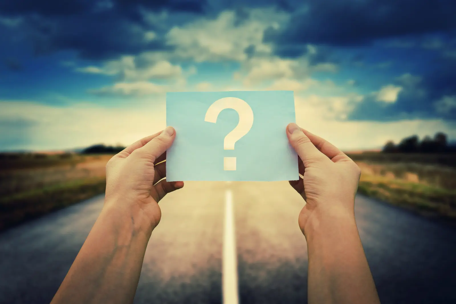 Hands holding a question mark card over a road for travel riddles and brain teasers
