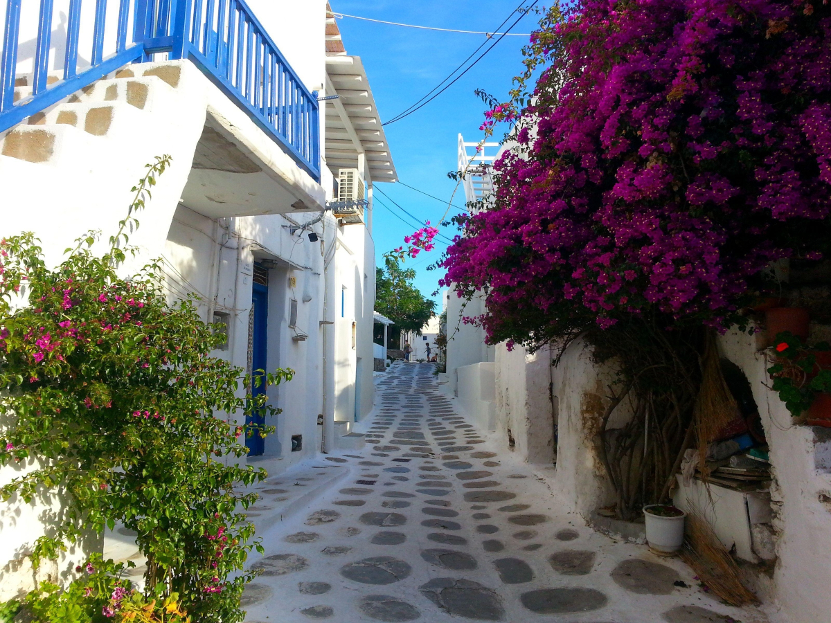 Whitewashed street in Mykonos, Greece, with blue balcony and bougainvillea, representing Greek wisdom and everyday culture