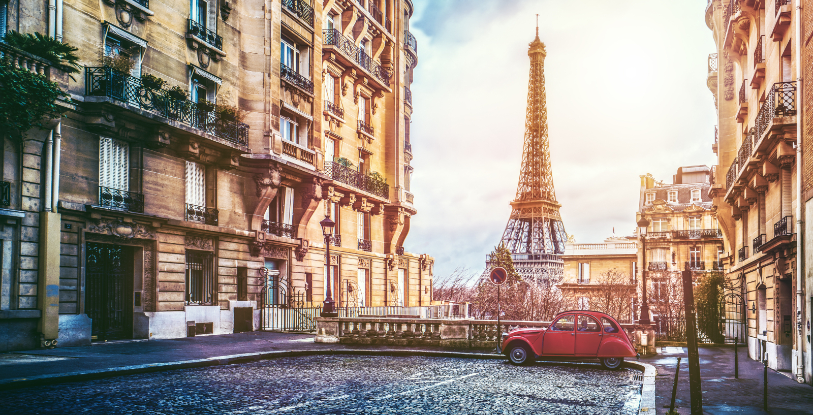 Classic historic architecture on a charming side street in Paris France with a vintage red car and a clear view of the Eiffel Tower highlighting local French culture.