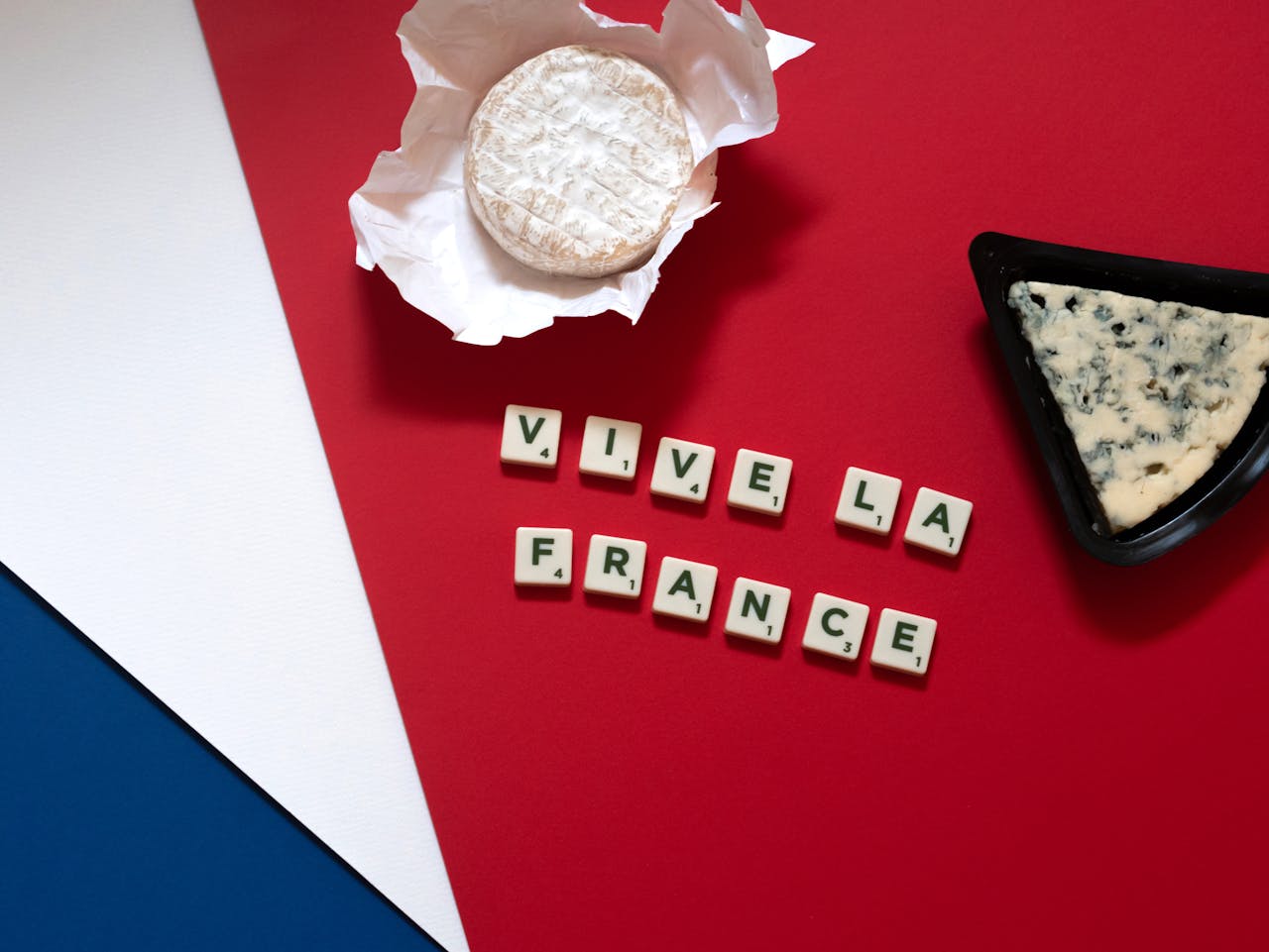 French cheese flat lay with Camembert and blue cheese on a blue, white, and red background next to scrabble tiles spelling Vive La France.