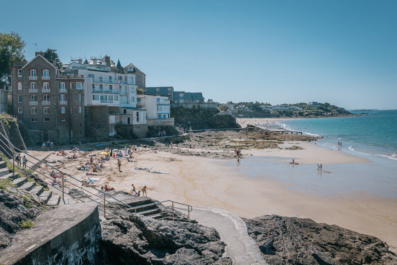 Rocky coastline and historic stone buildings overlooking a scenic sandy beach on a clear blue day in Brittany France representing regional French nature.