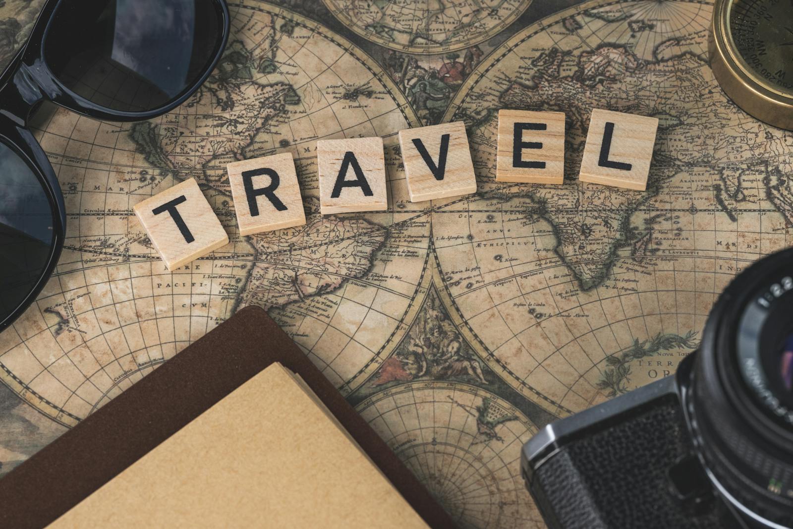 Travel word on a vintage world map with camera and notebook