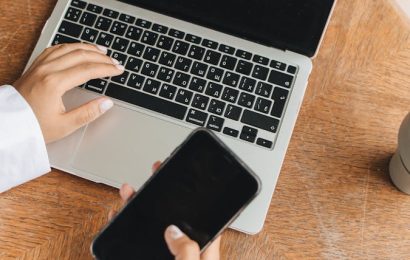 Person holding a phone with a dark screen near a laptop, showing why you should never keep important files only on your phone