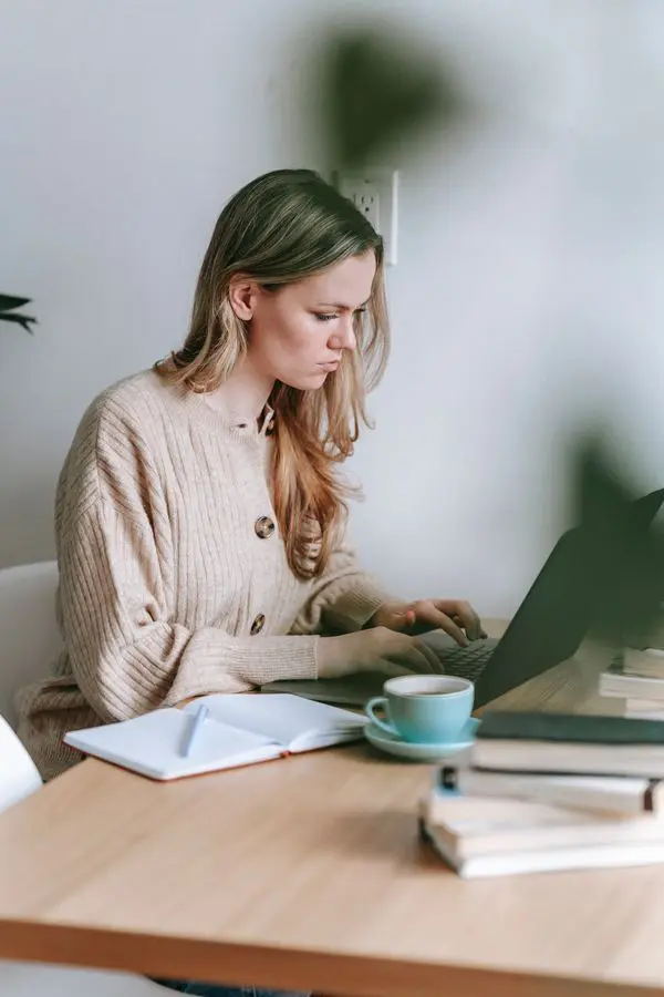 Woman using a laptop and notebook to prioritize a crowded to-do list with AI prompts