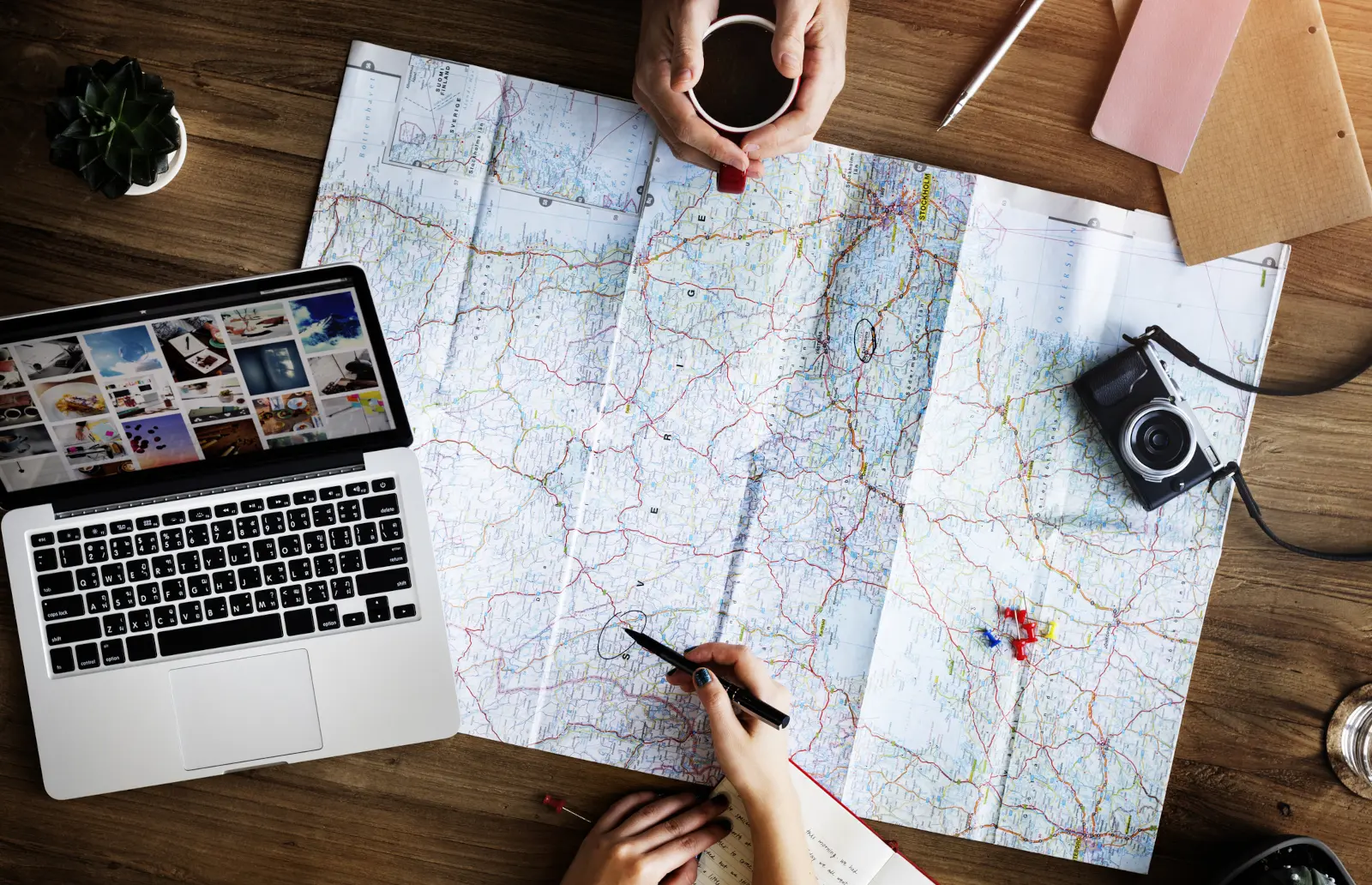 Travelers checking a paper map and laptop while planning routes and hotel locations before a trip