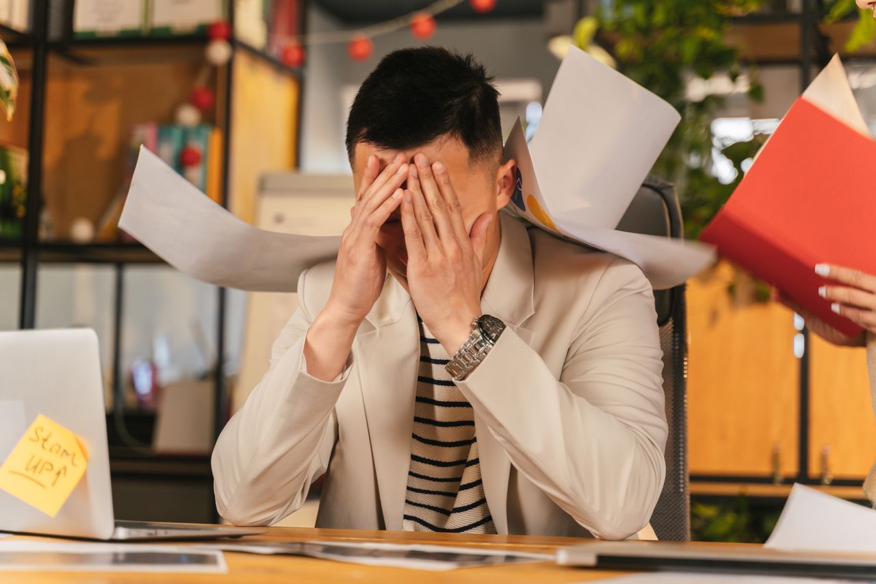 Overwhelmed office worker with papers around him after a small favor turns into extra work