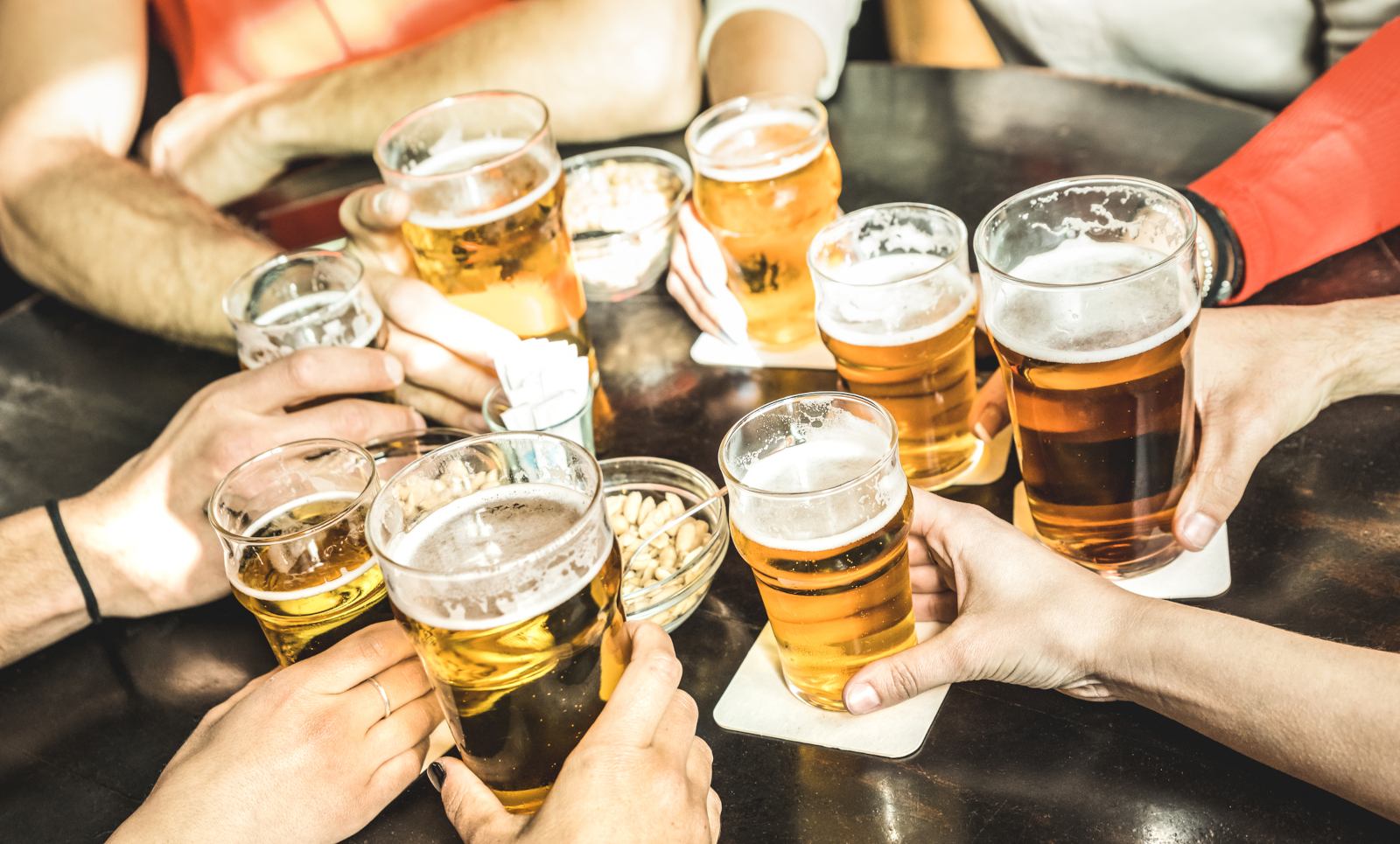 Friends raising glasses of beer together at a pub table - German Proverbs About Love, Friendship, and Family