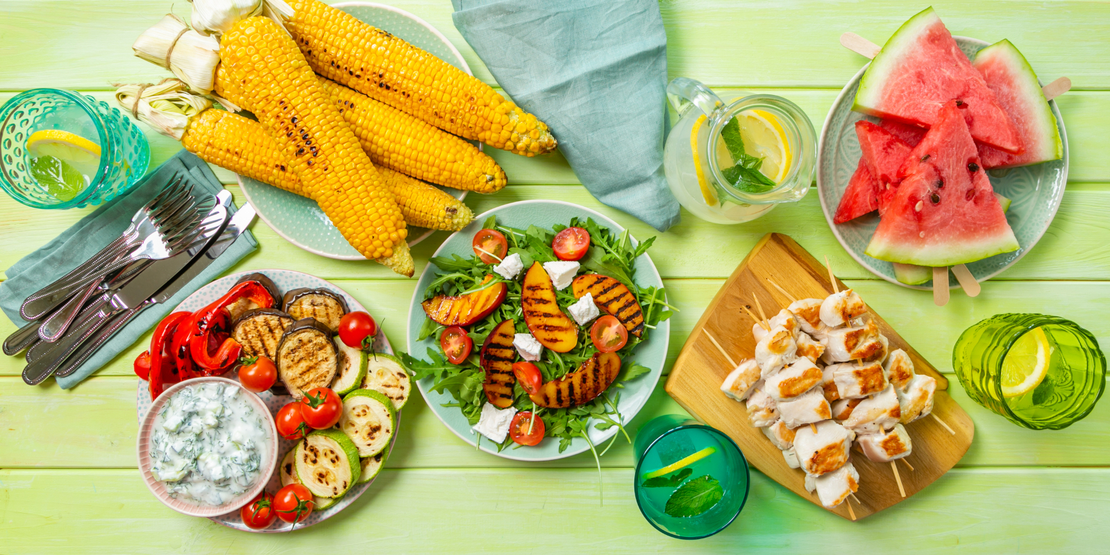 Summer barbecue spread with grilled chicken, corn, vegetables, salad, watermelon, and lemonade