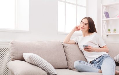Woman holding a smartphone while sitting on a sofa and thinking