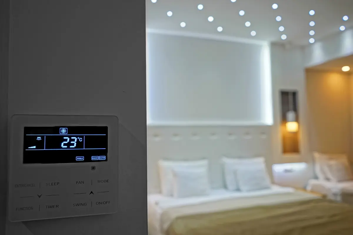 Hotel room air-conditioning thermostat set to 23°C with bed in background