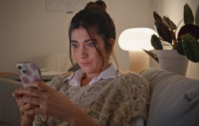 Woman relaxing on a sofa at night while using her smartphone