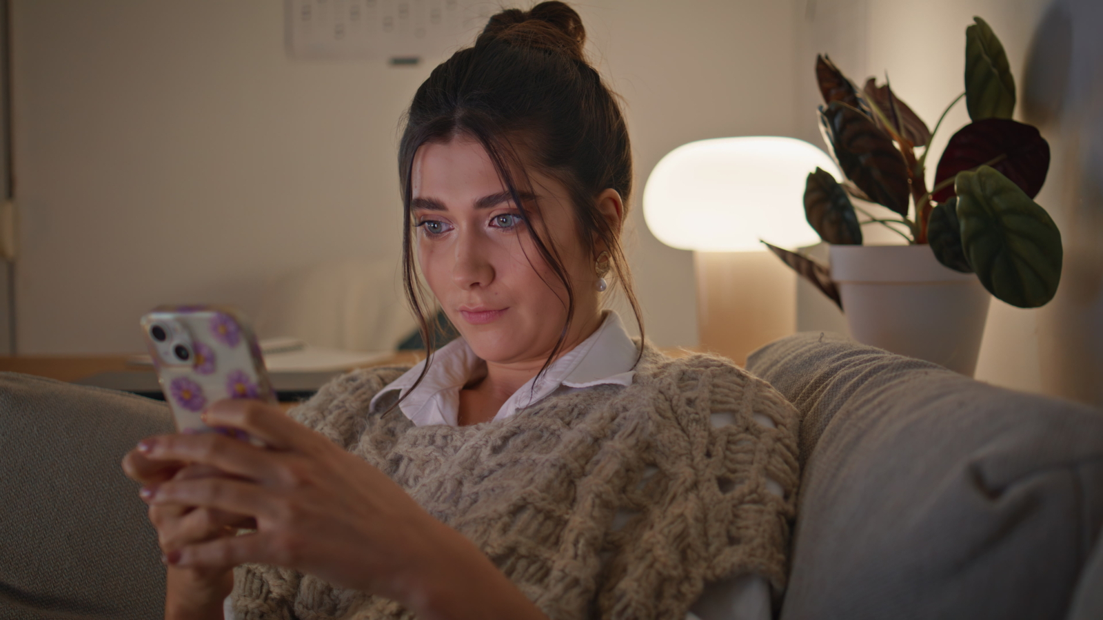 Woman relaxing on a sofa at night while using her smartphone