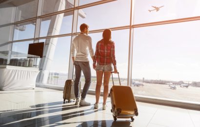 Couple with suitcases watching an airplane through an airport terminal window