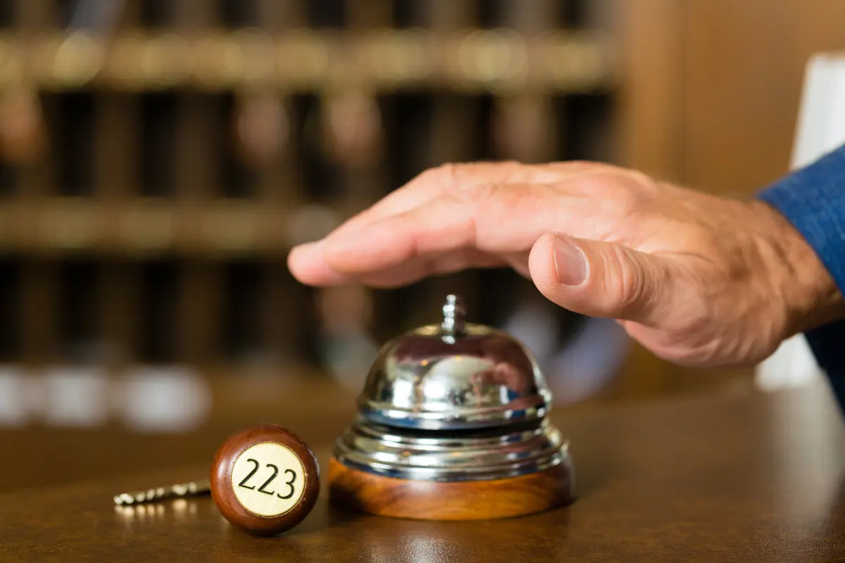 Guest ringing a hotel front desk bell beside a room key