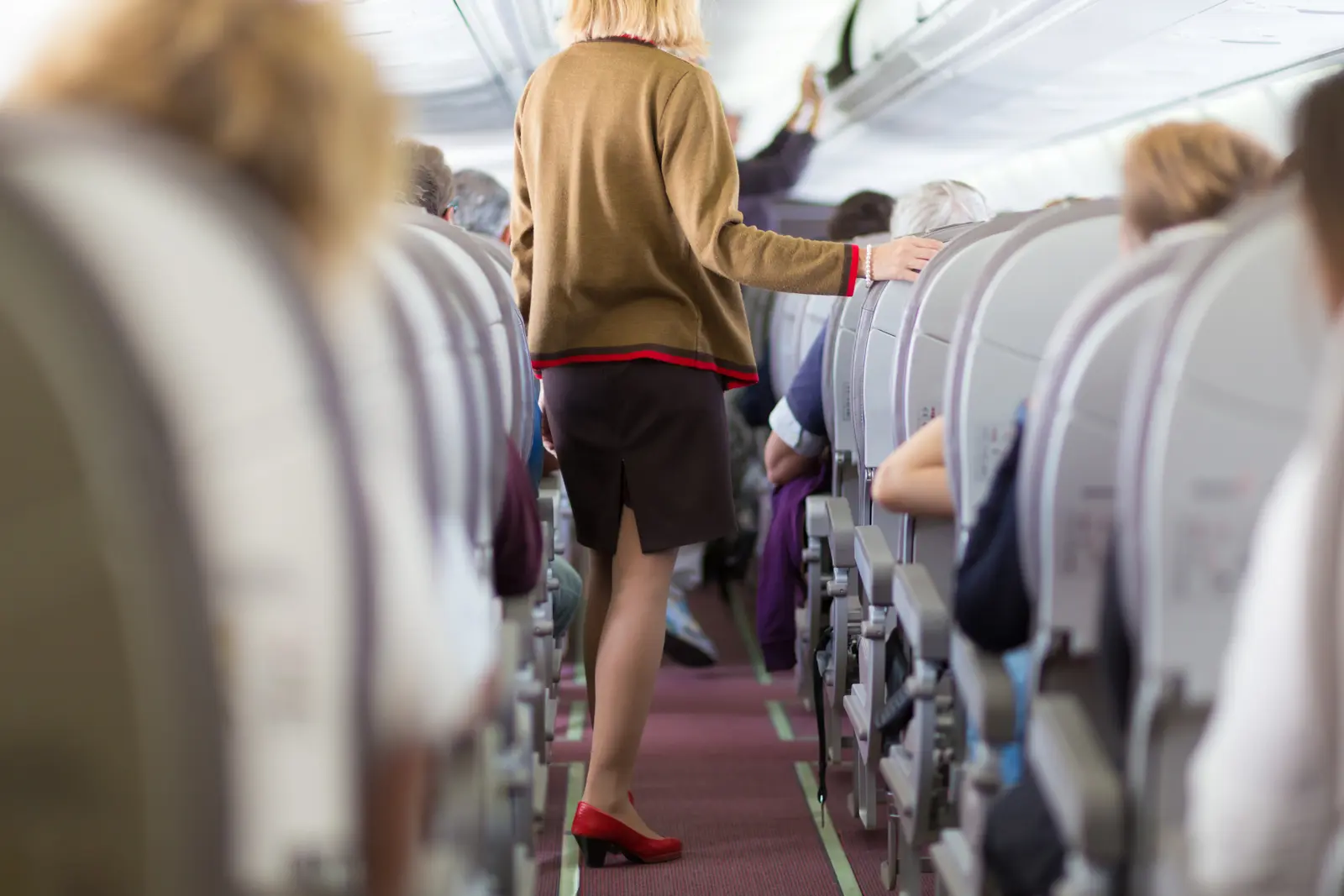Flight attendant walking through an airplane cabin with passengers seated
