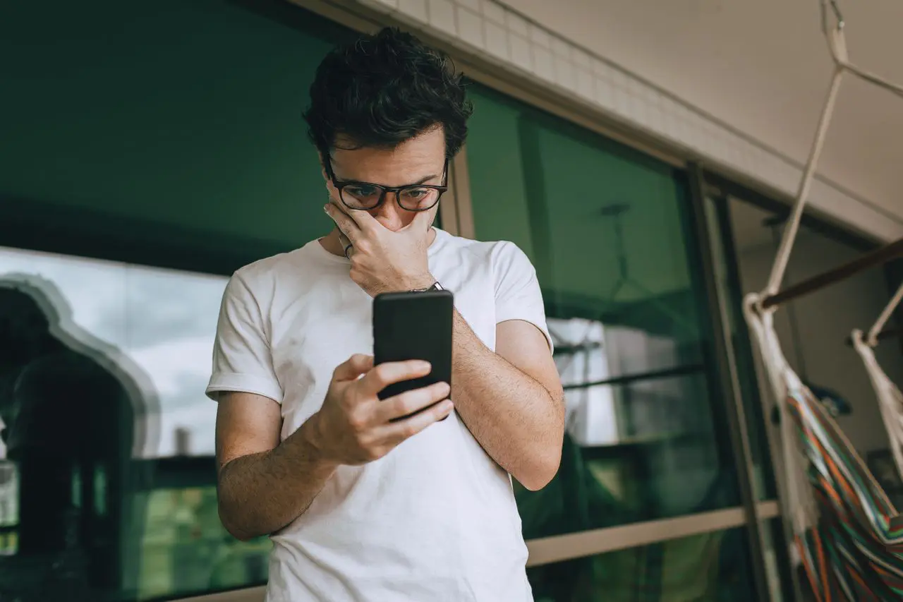 Contemplative Man looking at his phone with his hand against his face