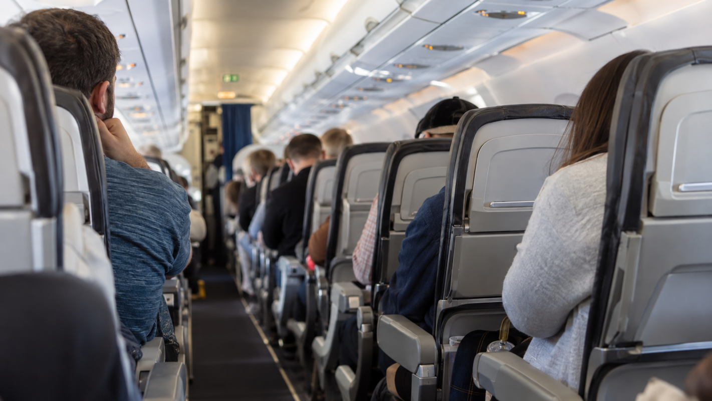 Passengers seated inside a commercial airplane cabin, viewed from behind