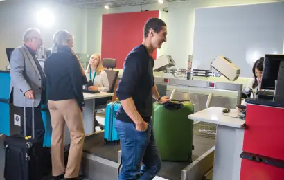 Male and female airline passengers having their luggage weighed at an airport check-in counter