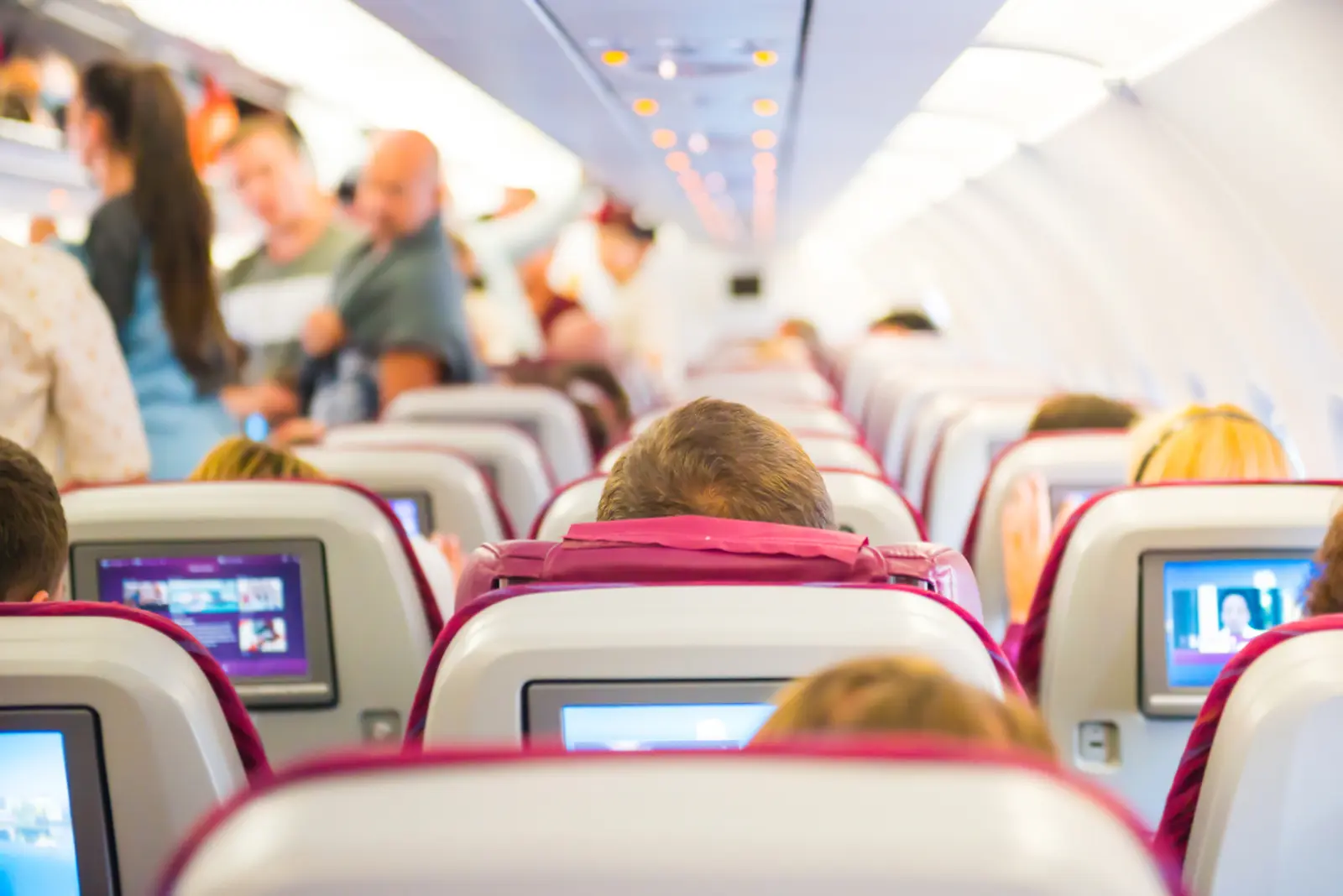 Passengers seated inside an airplane cabin as travelers move through the aisle before takeoff