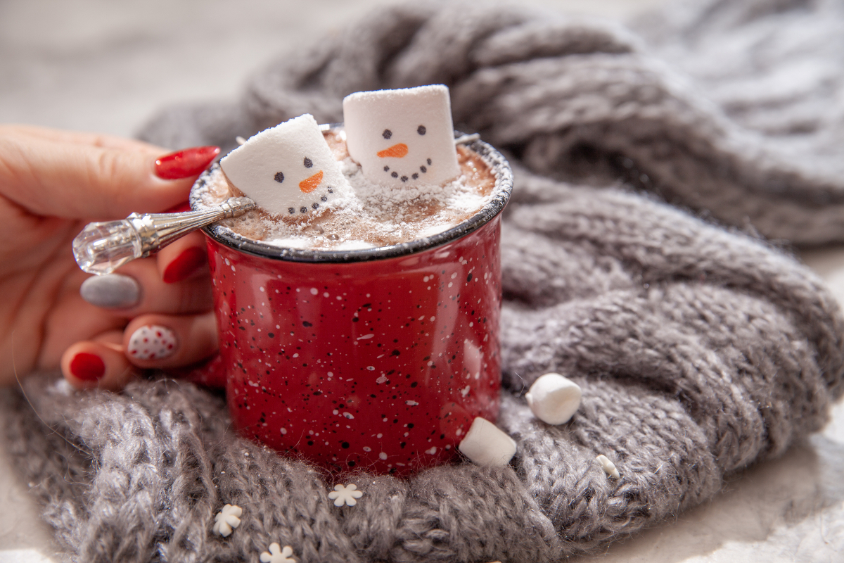 Woman holding a red mug of hot chocolate topped with a melting marshmallow snowman, a cozy winter treat.