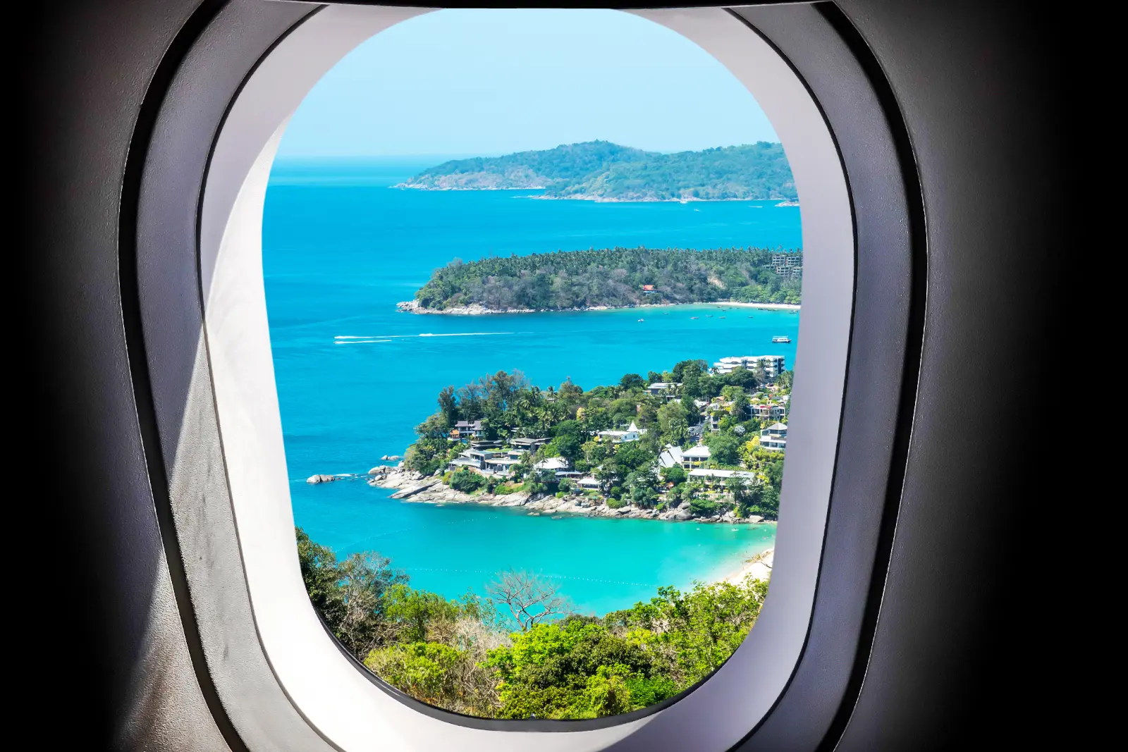Turquoise ocean and coastline seen through an airplane window during a daytime flight.