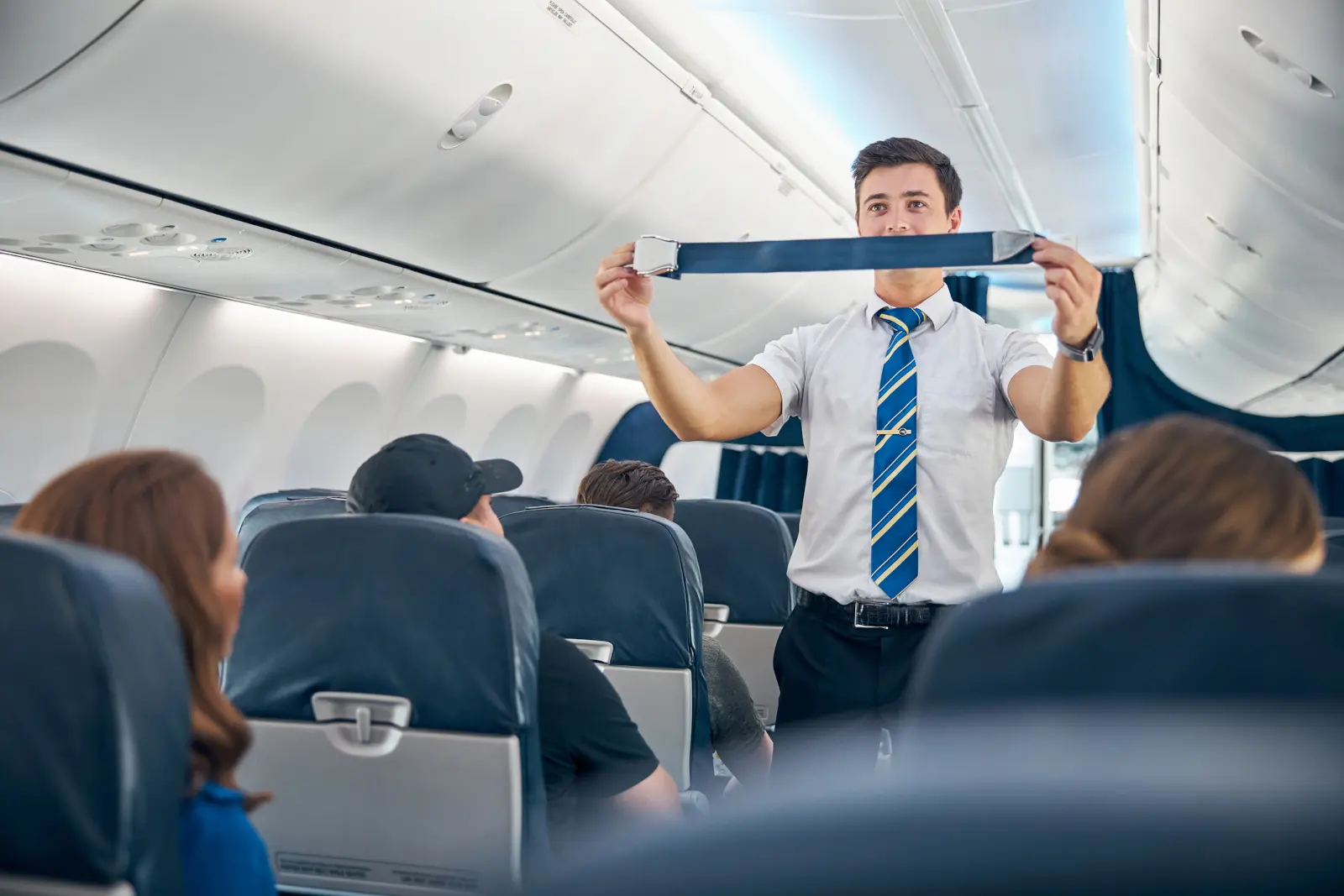 Male flight attendant demonstrating safety procedures inside an airplane cabin