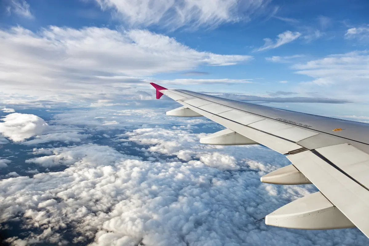 Airplane wing surrounded by white clouds, seen from a passenger window during a daytime flight.