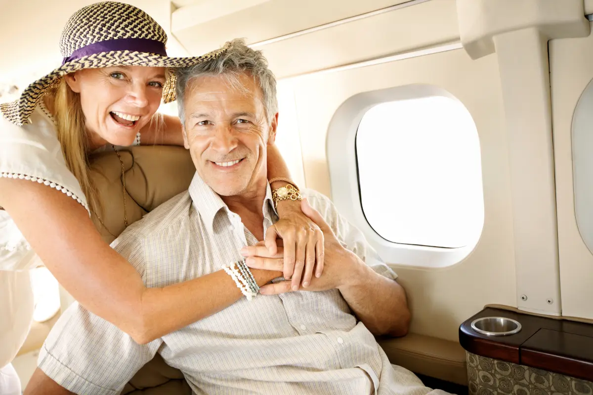 Smiling senior couple holding hands while sitting next to each other on an airplane