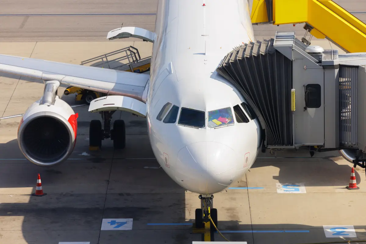 Passengers boarding airplane at airport gate with ground crew nearby