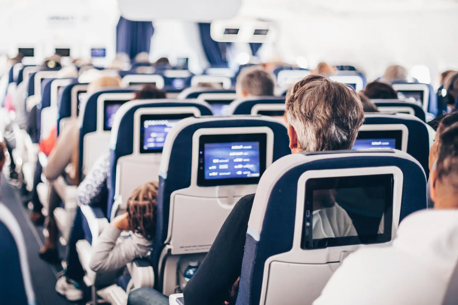 Flight attendant walking down the aisle of a commercial airplane with passengers seated on both sides