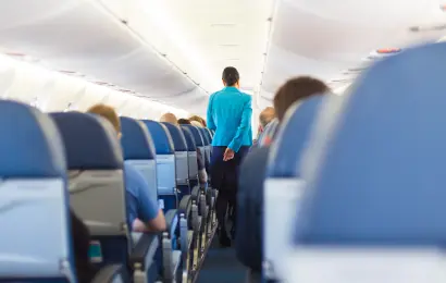 Flight attendant walking down the aisle of a commercial airplane with passengers seated on board.